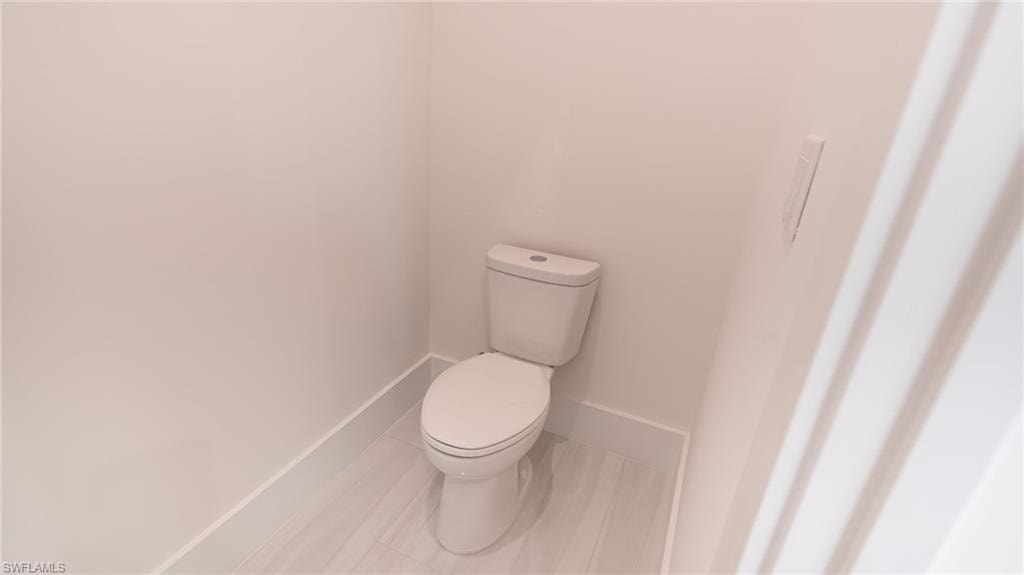 Powder room featuring a white toilet, light-toned walls, and wood-finish flooring with white baseboards
