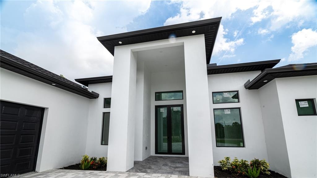 Contemporary exterior featuring a deep overhang entry, black-framed windows, dark roofing, and a patterned garage door