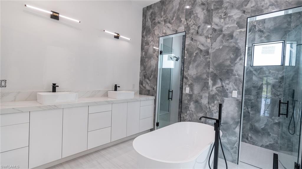 Spacious bathroom featuring a white freestanding soaking tub, dual glass-enclosed showers, and a double vanity with white cabinetry and rectangular vessel sinks