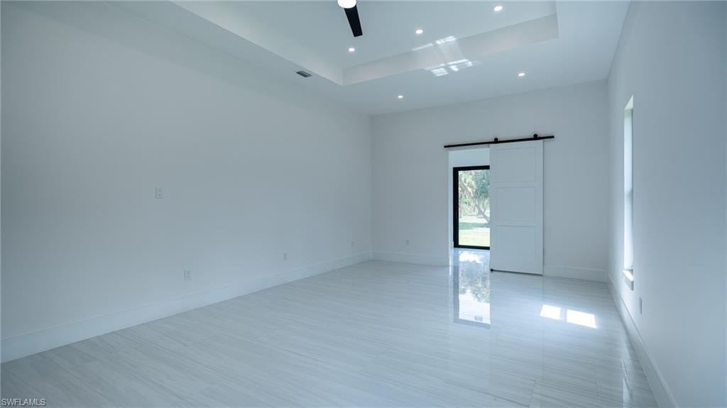 Spacious room featuring large format tile flooring, a tray ceiling with recessed lighting, and a modern barn door entry to an outdoor area
