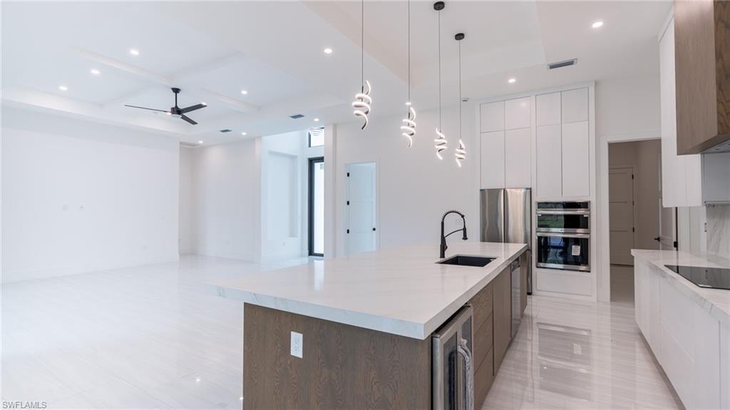 Open-concept kitchen and living area featuring a large center island with integrated sink and beverage cooler, stainless steel appliances, white flat-panel cabinetry, and recessed lighting