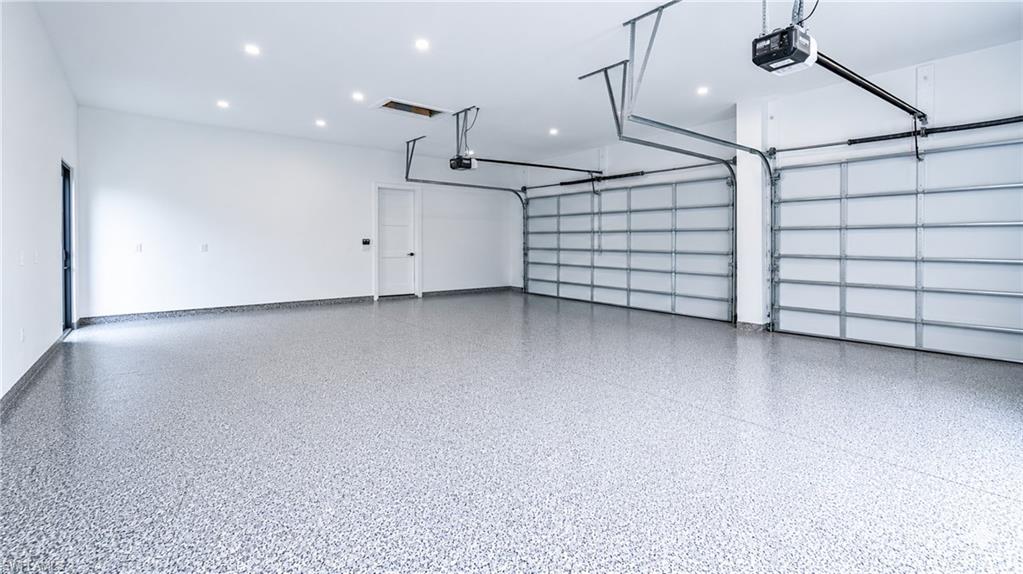 Spacious garage featuring a durable epoxy floor finish, recessed ceiling lighting, two automatic garage doors, and a pedestrian door