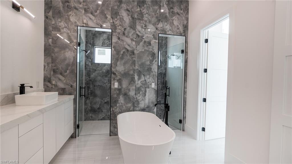 Contemporary bathroom featuring a freestanding tub, two glass-enclosed showers, a double vanity with stone countertops, and large format wall tiling