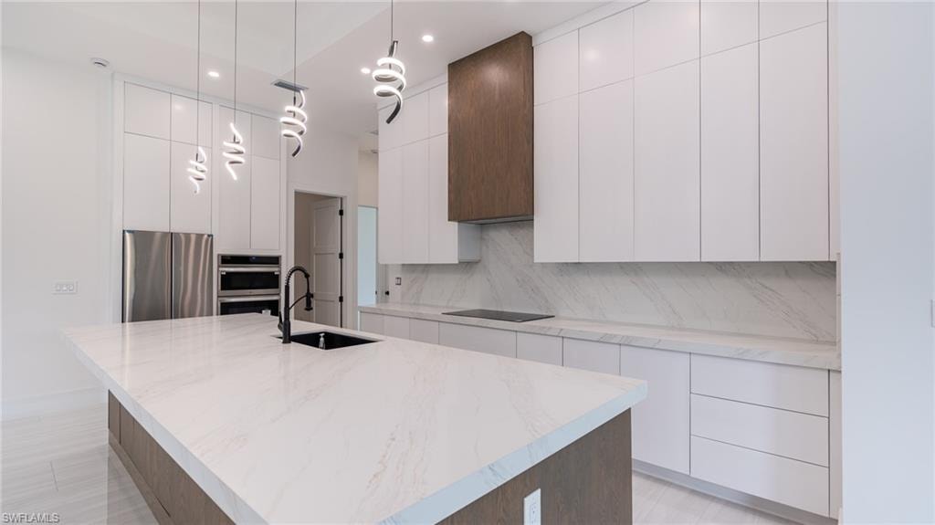 Contemporary kitchen featuring a large island with an undermount sink, white flat-panel cabinetry, stainless steel appliances, a wood-finish range hood, and modern pendant lighting