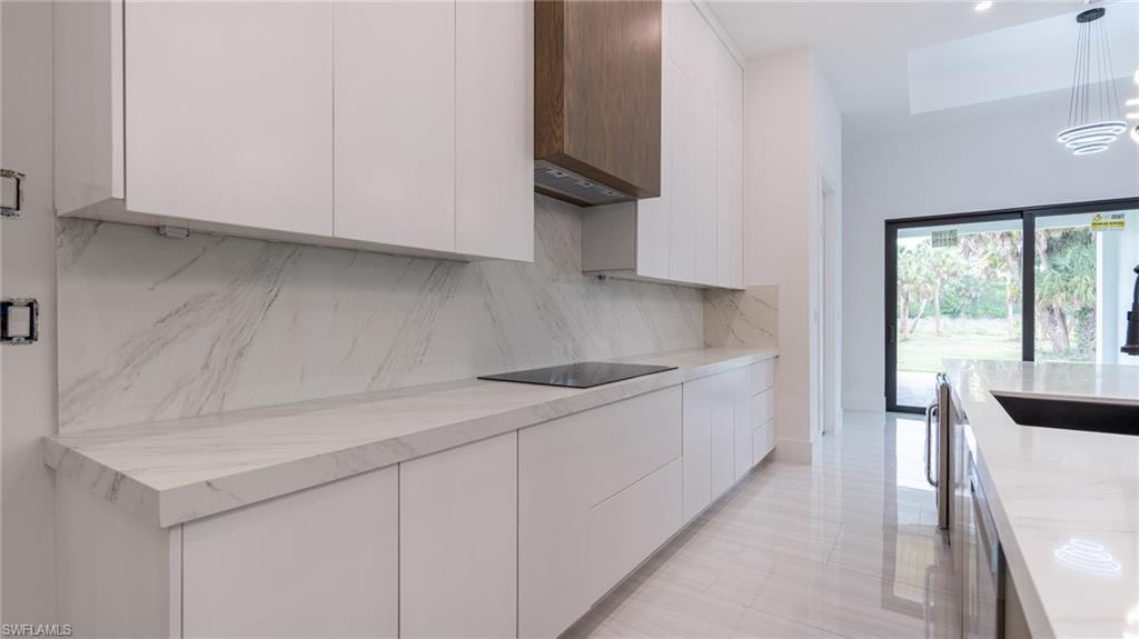 Modern kitchen featuring white flat-panel cabinetry, a wood-finish range hood, and a built-in cooktop