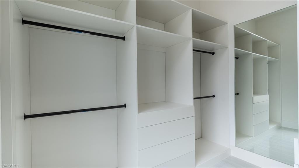 Built-in closet system featuring white cabinetry, multiple hanging rods, diverse shelving, integrated drawers, and a full-length mirrored panel