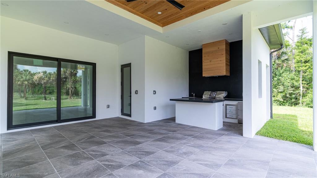 Covered patio featuring an outdoor kitchen with integrated grill and beverage refrigerator, wood-finish ceiling, and dark gray porcelain tile flooring