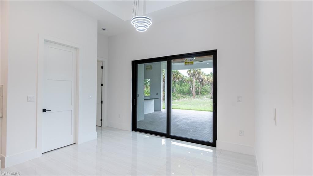 Spacious interior featuring a large sliding glass door, high ceilings, bright white walls, polished tile flooring, and a contemporary chandelier