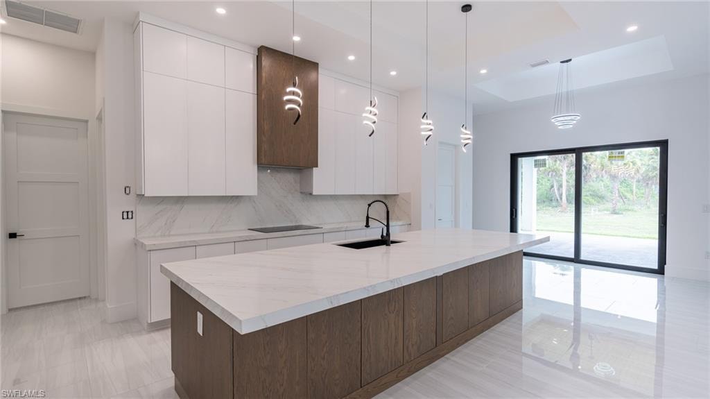 Modern kitchen featuring a large central island with a light-colored countertop, contrasting dark wood-finish cabinetry, a sleek black faucet, and contemporary pendant lighting