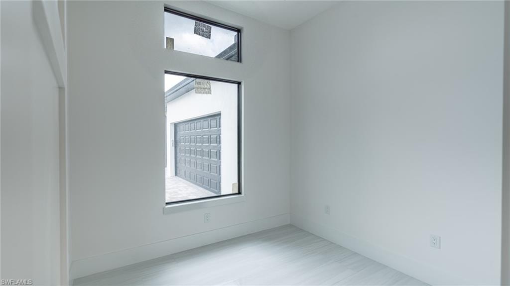 Bright interior room featuring a large rectangular window with transom, light wood-finish flooring, and crisp white walls