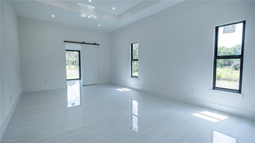 Spacious room featuring glossy tile flooring, recessed ceiling lighting, a tray ceiling, and a modern barn door