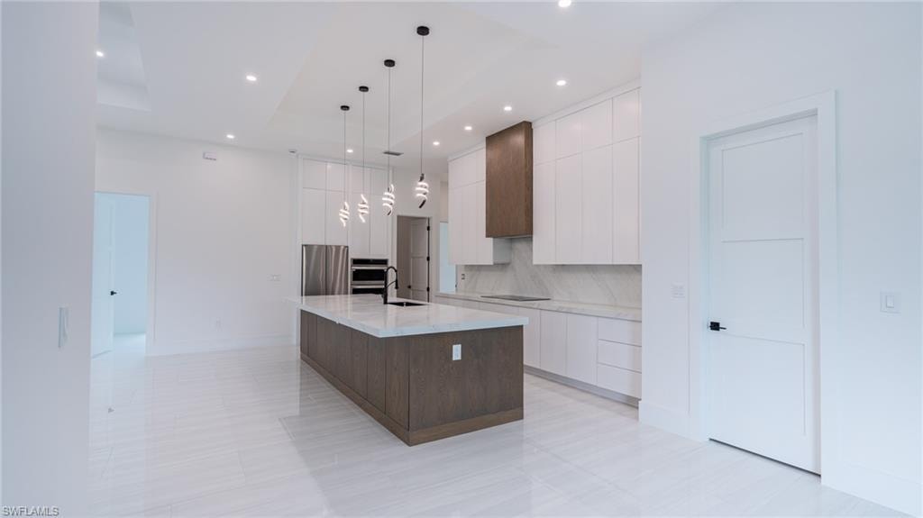 Modern kitchen featuring an expansive center island with a stone countertop, sleek white cabinetry, and a wood-finish range hood