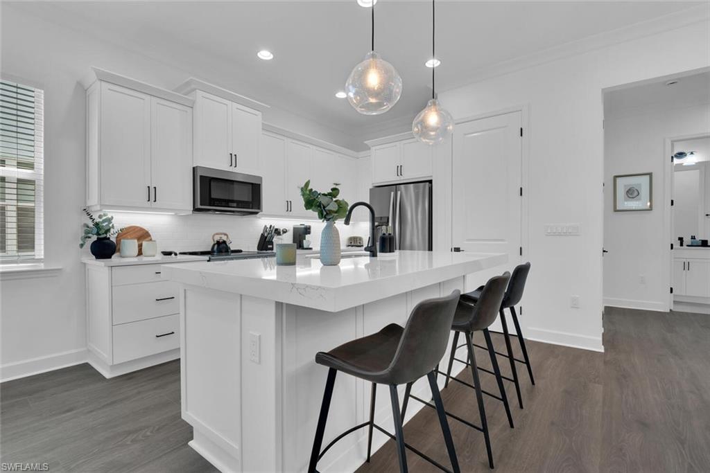 Kitchen with dark wood-type flooring, white cabinetry, a sink, stainless steel appliances, and backsplash