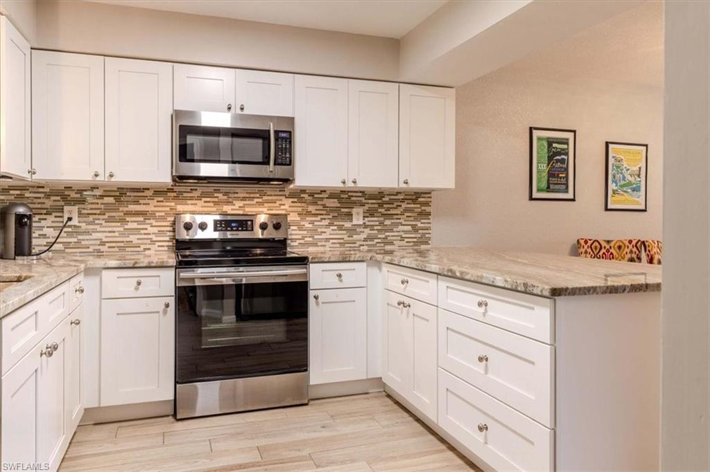 Kitchen with stainless steel appliances, white cabinetry, light stone countertops, and light wood-type flooring