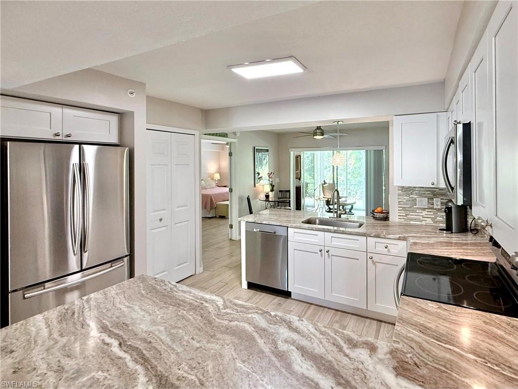Kitchen featuring a peninsula, stainless steel appliances, white cabinetry, light stone countertops, and decorative backsplash
