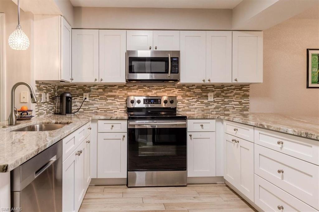 Kitchen with stainless steel appliances, white cabinetry, light stone countertops, and backsplash