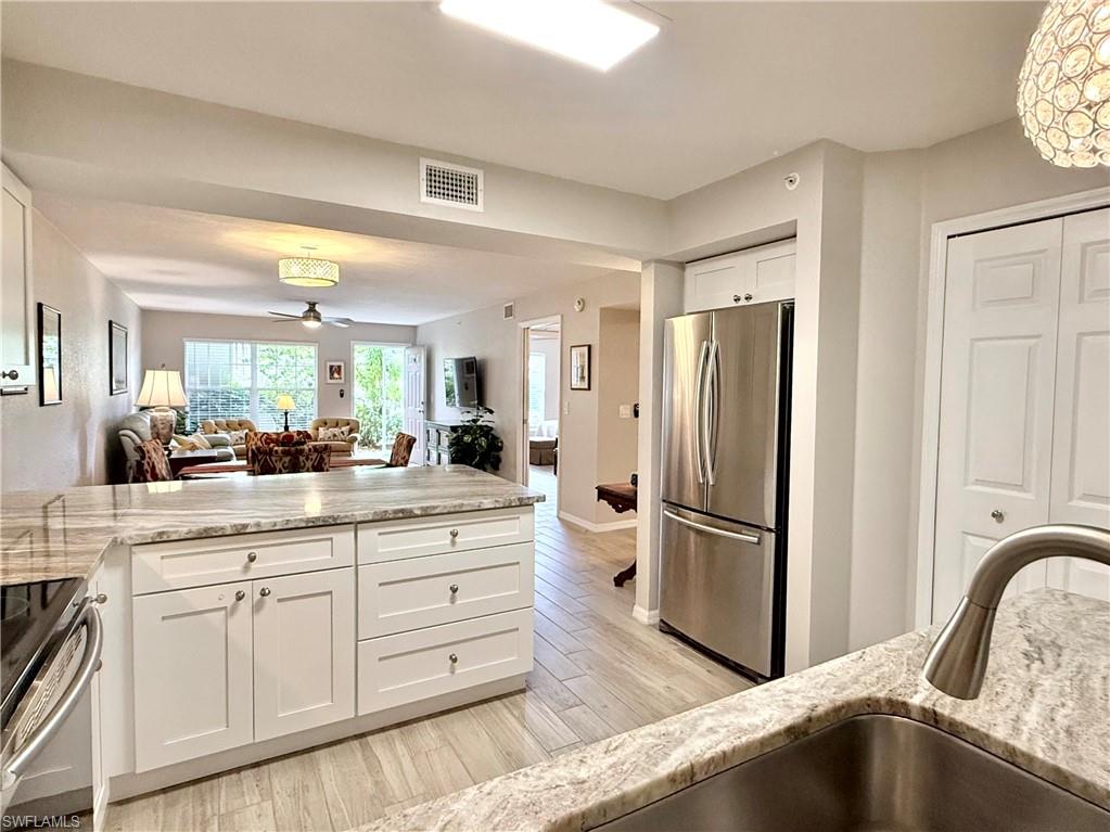 Kitchen with white cabinetry, open floor plan, stainless steel appliances, light stone counters, and a peninsula