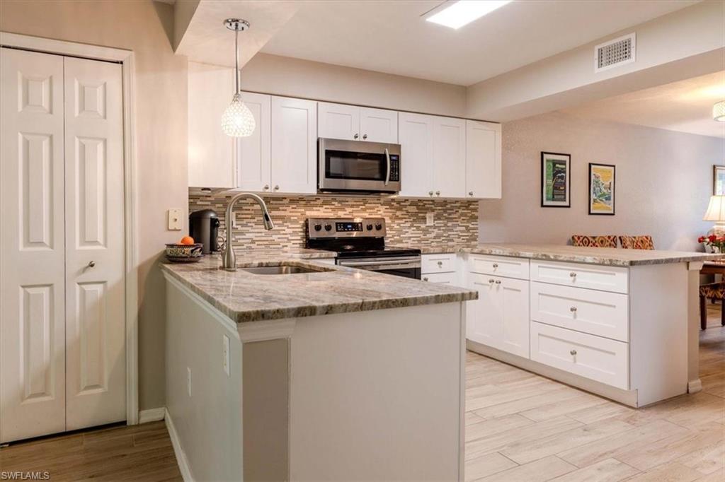 Kitchen featuring a peninsula, light stone countertops, white cabinets, hanging light fixtures, and stainless steel appliances