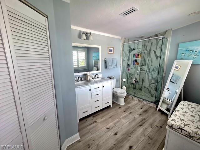 Primary Bathroom with a closet, double vanity, a marble finish shower, light wood-style floors, and ornamental molding