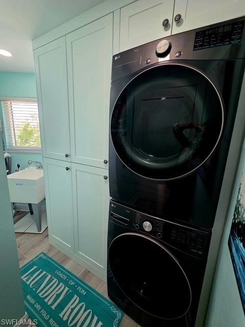 Laundry room featuring cabinet space, stacked washing machine and dryer, and light wood-style floors