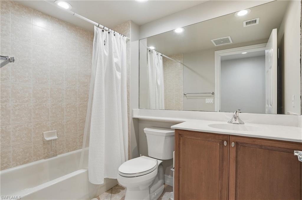Bathroom featuring a white bathtub, tiled shower walls, a vanity with a white countertop and brown cabinetry, and a large mirror