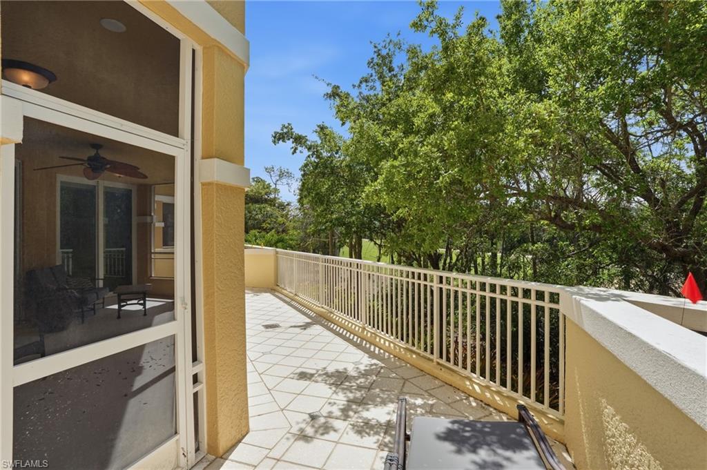 Expansive outdoor patio area featuring a tiled surface and a sturdy white railing, offering views of mature trees and landscaping