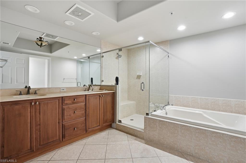 The bathroom features a double vanity with a light-colored countertop, a glass-enclosed shower, and a built-in bathtub