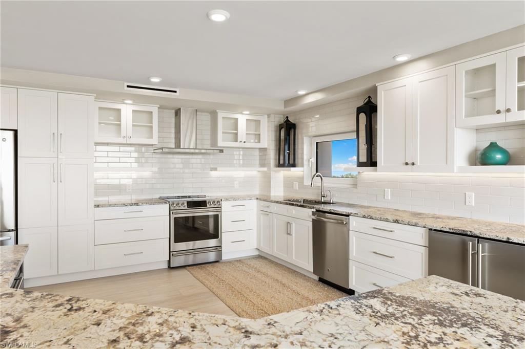 Kitchen with stainless steel appliances, wall chimney exhaust hood, a sink, decorative backsplash, and recessed lighting