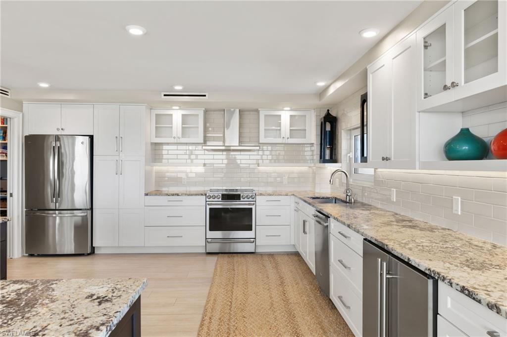 Kitchen featuring stainless steel appliances, a sink, wall chimney exhaust hood, decorative backsplash, and recessed lighting