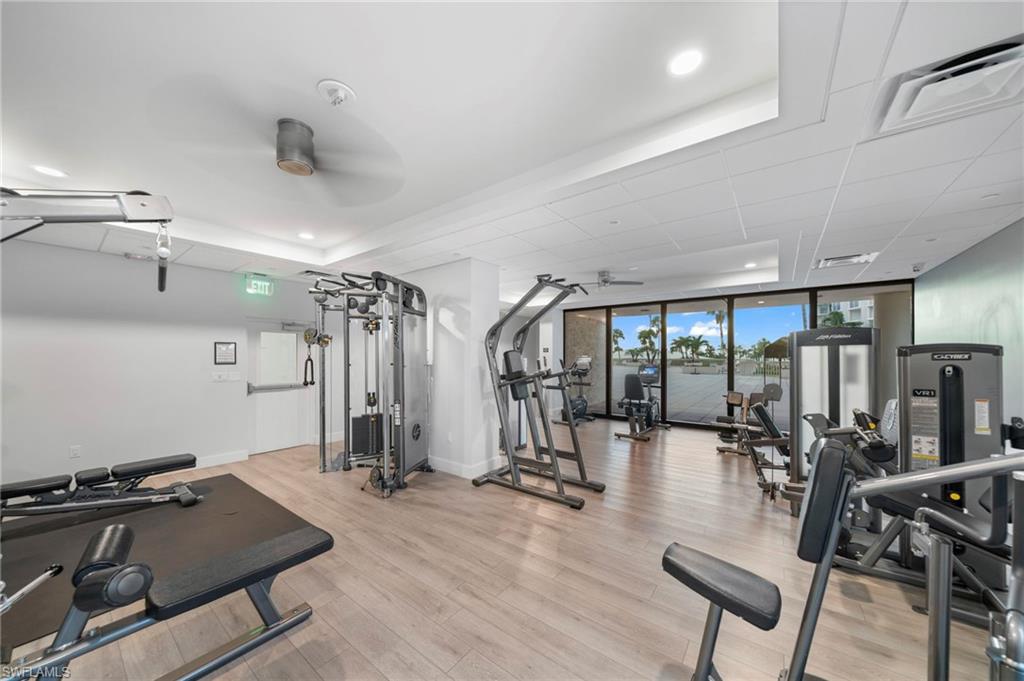 Gym featuring ceiling fan, a tray ceiling, light wood finished floors, baseboards, and recessed lighting
