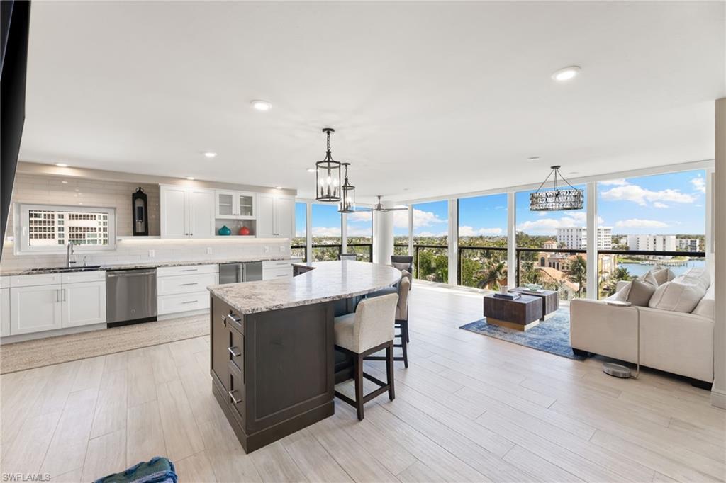 Kitchen with stainless steel dishwasher, a chandelier, white cabinets, light stone countertops, and a sink