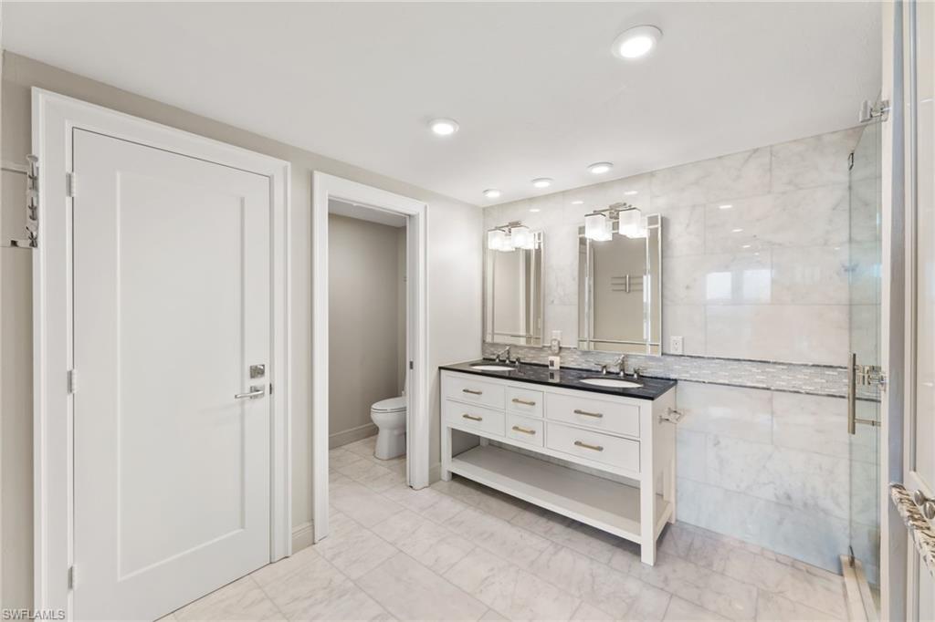 Bathroom featuring double vanity, toilet, marble finish floors, a shower stall, and baseboards
