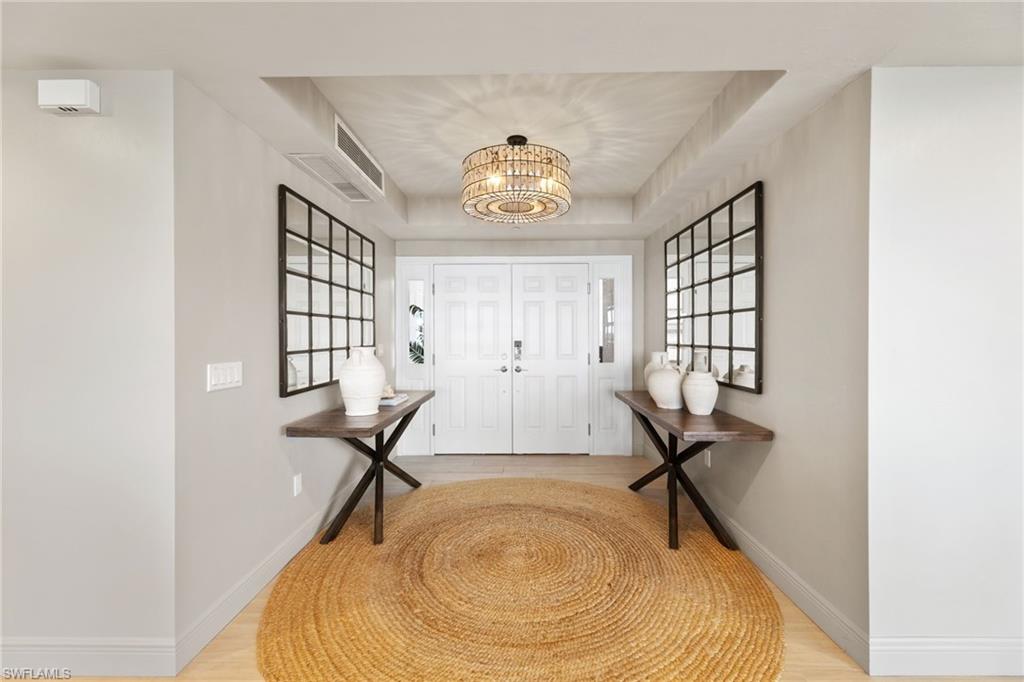 Entryway with a chandelier, baseboards, a raised ceiling, and light wood-style floors