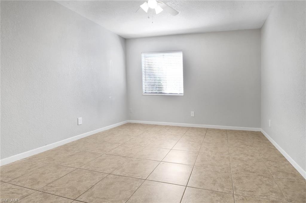 Spare room with light tile patterned floors, baseboards, and ceiling fan