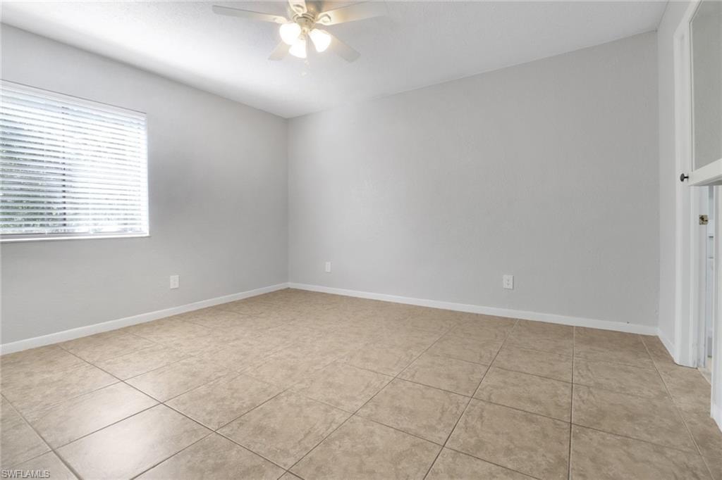Empty room with light tile patterned floors, baseboards, and ceiling fan