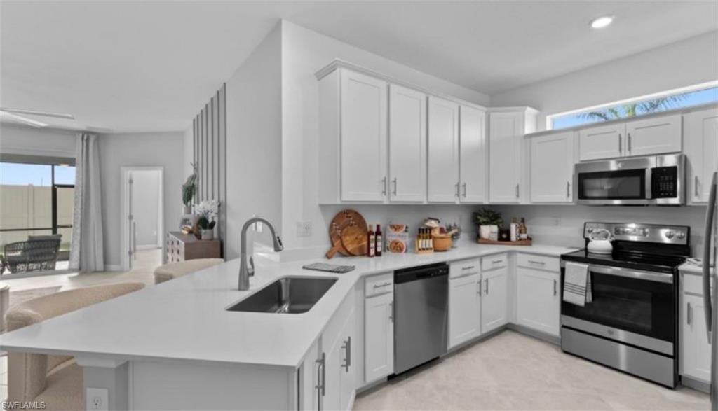 Kitchen with stainless steel appliances, a peninsula, white cabinets, and a breakfast bar area