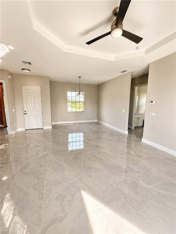Expansive living space featuring large-format tile flooring, a tray ceiling, and a contemporary ceiling fan
