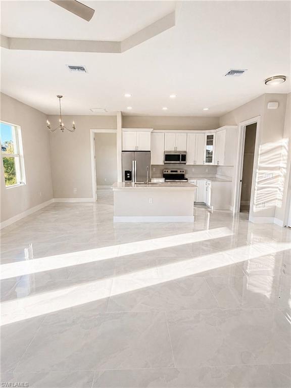 Spacious kitchen and living area featuring large format tile flooring, a kitchen island with seating, stainless steel appliances, white cabinetry, and recessed lighting