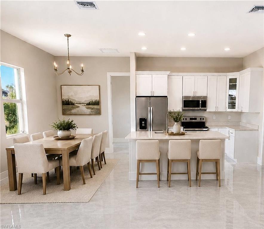 Open-concept design featuring a central kitchen island with seating, stainless steel appliances, white cabinetry, and light-toned flooring