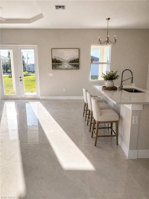 Spacious interior featuring large format tile flooring, a kitchen island with seating, pendant lighting, and double glass-paneled doors opening to the exterior