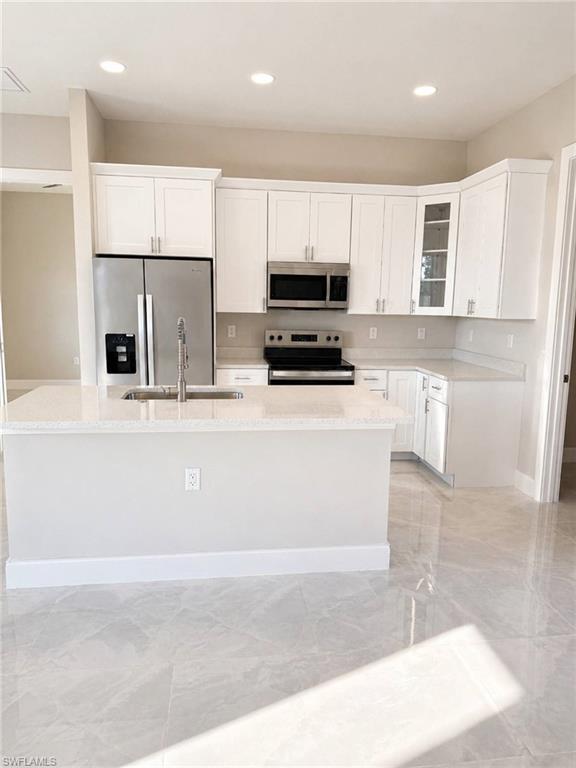 Modern kitchen featuring white shaker cabinetry, stainless steel appliances, a center island with sink, light-toned countertops, and large format tile flooring