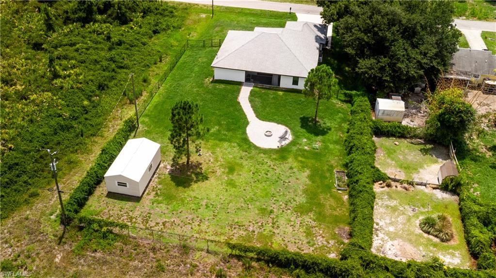 Expansive fenced grounds featuring a gravel fire pit area, two mature trees, and a detached white storage building