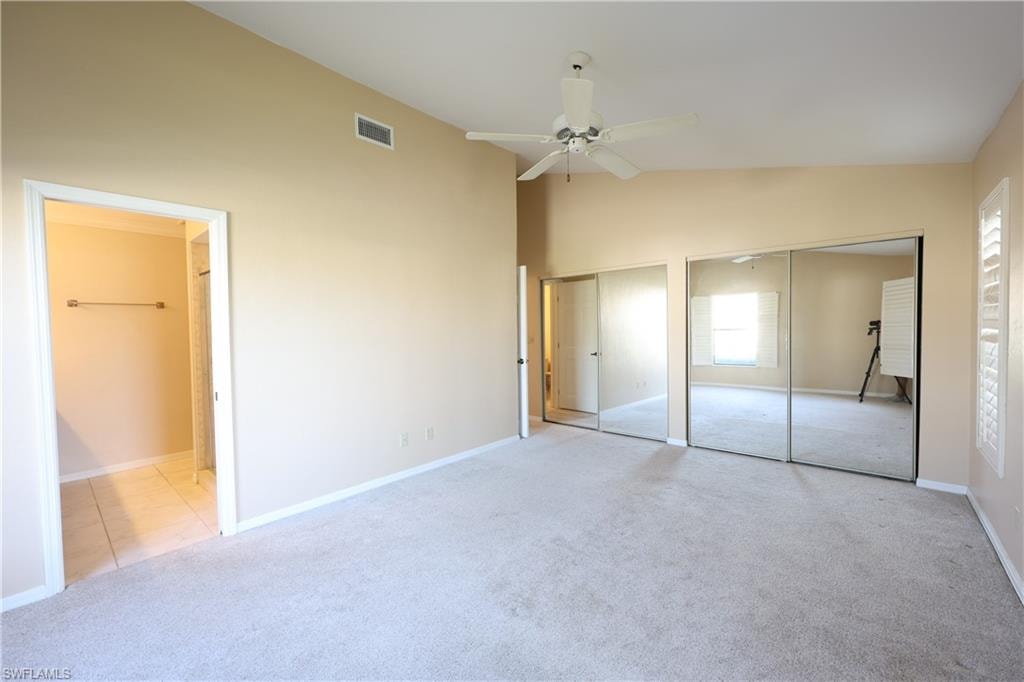 Unfurnished bedroom with two closets, lofted ceiling, light carpet, a ceiling fan, and connected bathroom