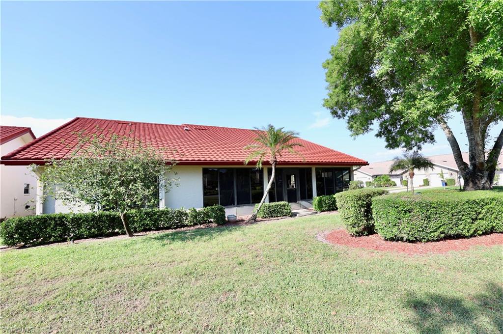 Rear view of house with a yard, a tile roof, a sunroom, and stucco siding