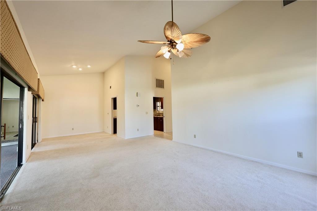 Empty room with light colored carpet, ceiling fan, and lofted ceiling