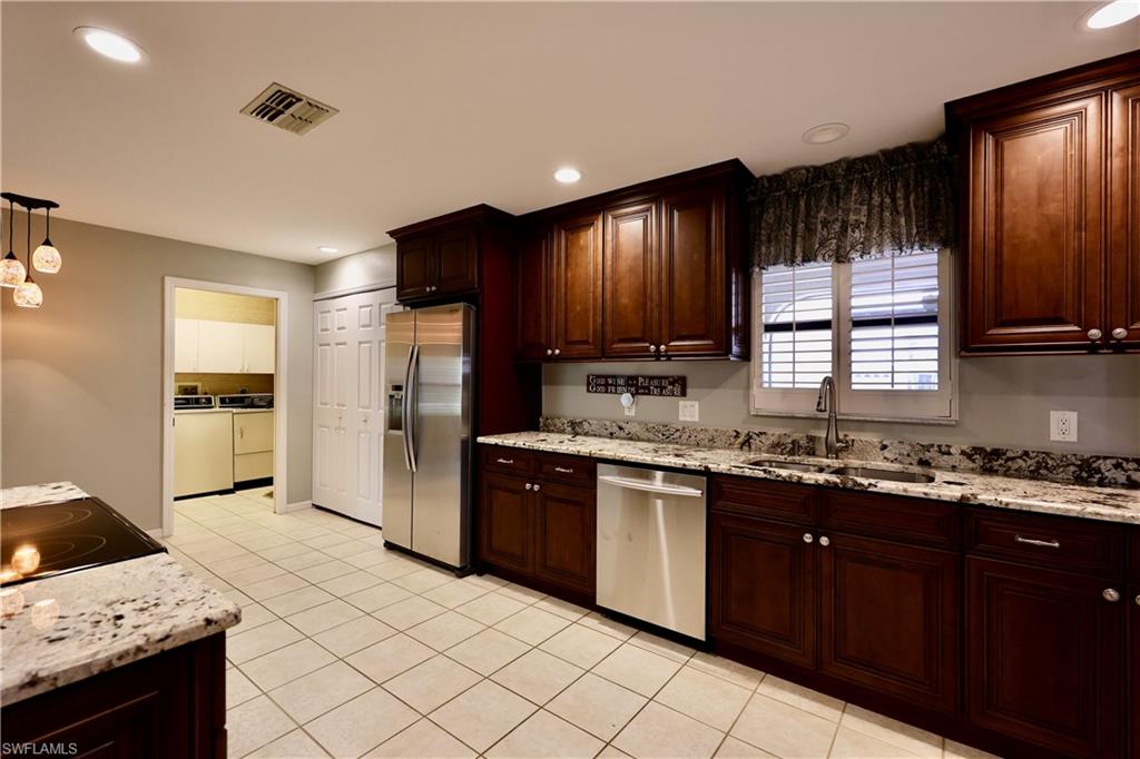 Kitchen with stainless steel appliances, light stone counters, dark wood finish cabinetry, and decorative light fixtures