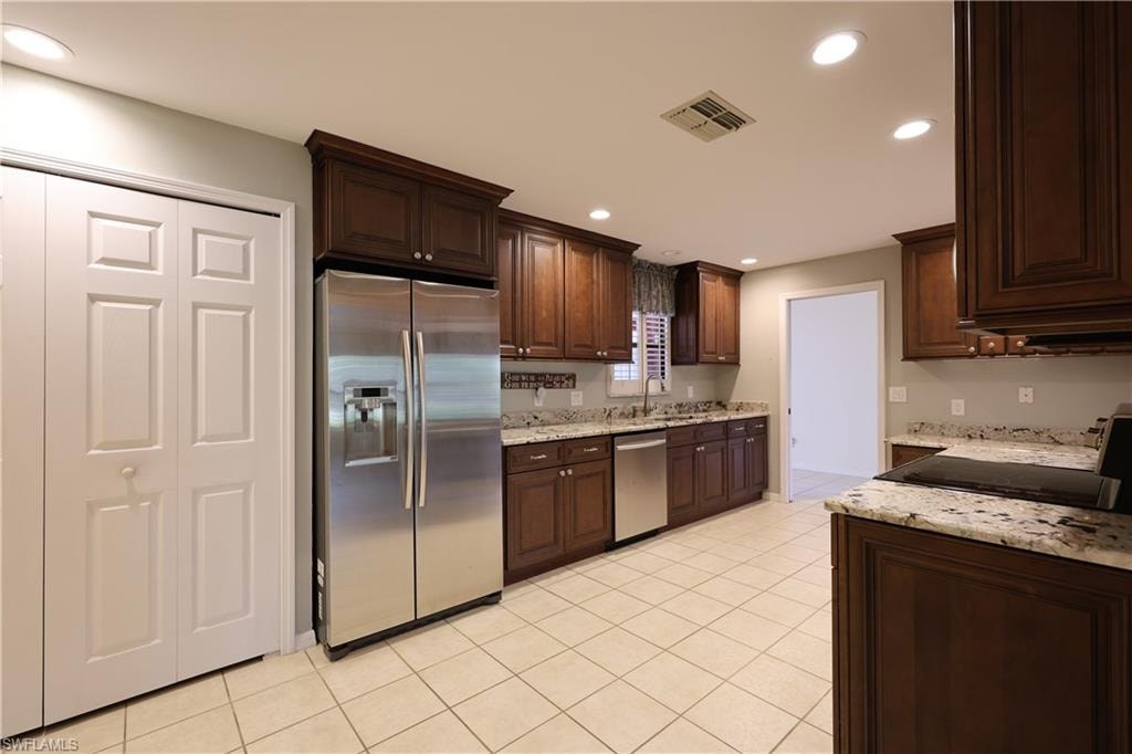 Kitchen with stainless steel appliances, dark wood finish cabinets, light stone counters, recessed lighting, and light tile patterned floors