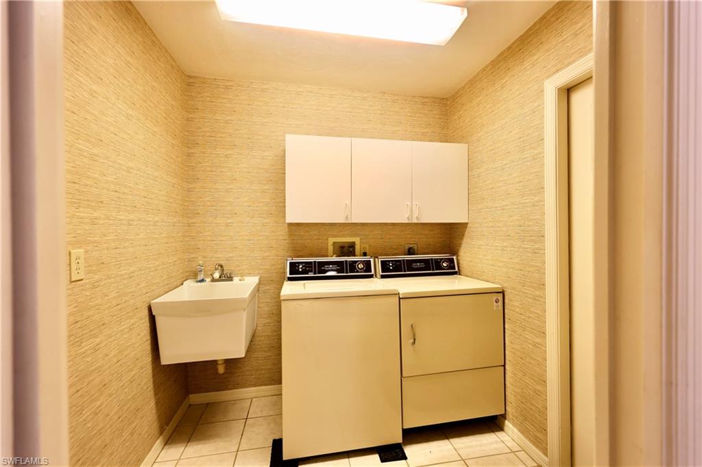 Laundry room with wallpapered walls, washer and dryer, light tile patterned floors, and cabinet space