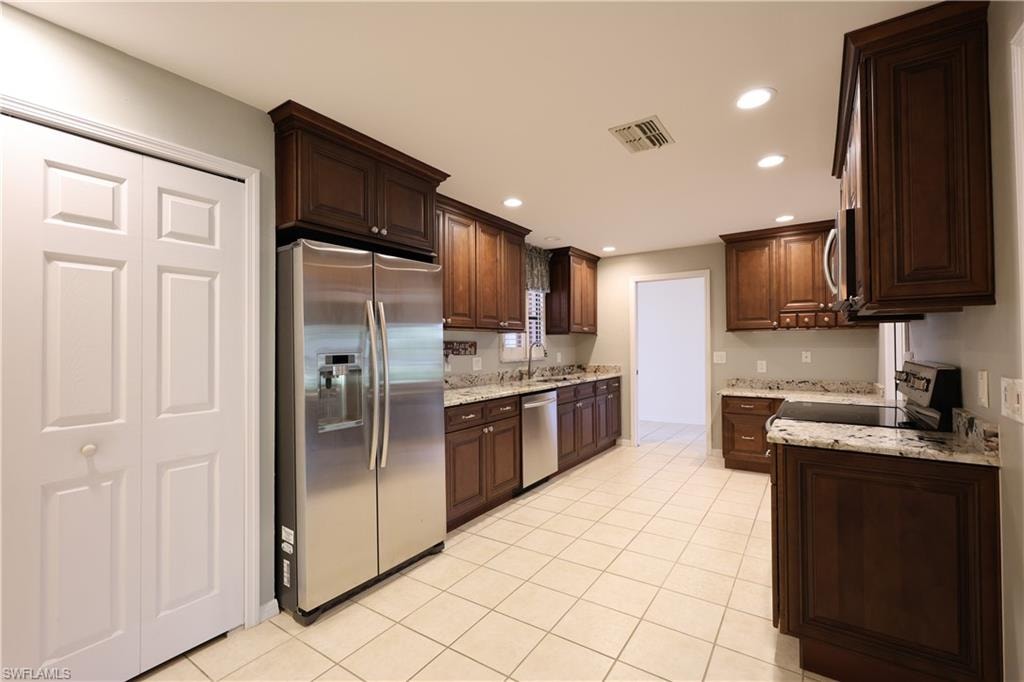 Kitchen featuring stainless steel appliances, light stone counters, dark wood finish cabinets, recessed lighting, and light tile patterned floors