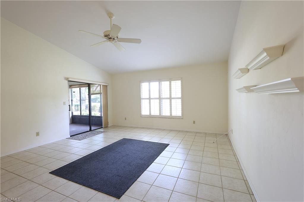 Empty room with a ceiling fan, lofted ceiling, and light tile patterned floors